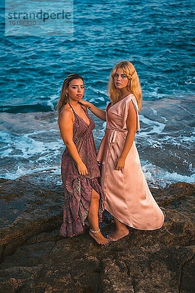 Romantische Blicke eines Paares von kaukasischen Mädchen in rosa Kleidern  posiert Sommer am Strand am Meer