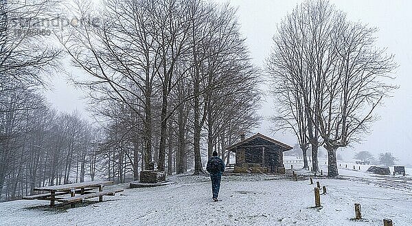Ein junger Mann zu Fuß neben der Hütte des Mount Aizkorri in Gipuzkoa. Verschneite Landschaft bei Winterschnee. Baskenland  Spanien  Europa
