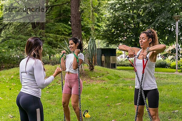 Latino Mädchen beim Sport in einem grünen Park  Lifestyle ein gesundes Leben  Lehrer mit den Schülern  die mit elastischen Bändern trainieren