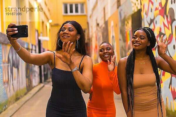 San Sebastián  Gipuzkoa Spanien  Februar 2021: Drei Mädchen machen ein Selfie. Modischer urbaner Stil mit drei schwarzafrikanischen Mädchen auf einer Stadtstraße  enge Kleider