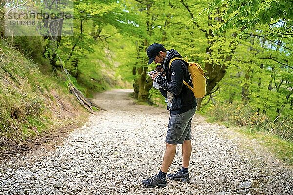 Ein junger Vater  der sein neugeborenes Kind auf einem Waldweg auf dem Weg zum Picknick mit der Familie gut im Rucksack verstaut