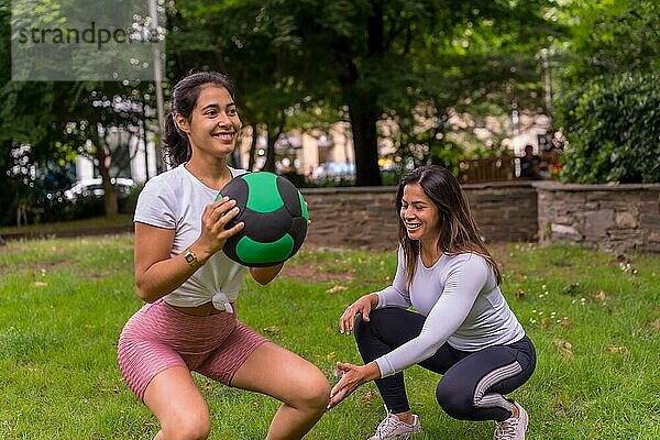 Lateinisches Mädchen beim Sport in einem grünen Park  Lebensstil ein gesundes Leben  aufmerksamer Lehrer mit den Schülern bei der Übung von Kniebeugen mit dem Gewichtsball