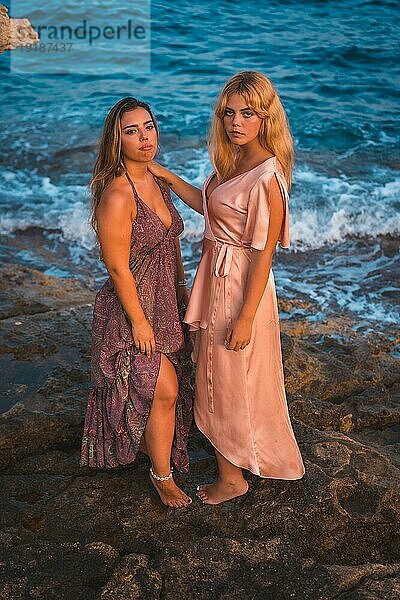 Ein paar kaukasische Mädchen in rosa Kleidern  posieren Sommer am Strand am Meer