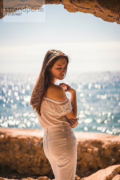 Lebensstil eines jungen rothaarigen  weiß gekleideten Mädchens an einem Sommermorgen neben einem Felsen am Meer