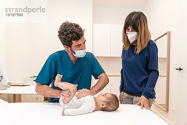 Frontalaufnahme eines jungen Arztes und einer Mutter bei einer Babyuntersuchung in einer Klinik