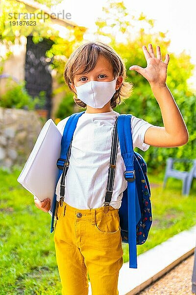 Kaukasisches Kind mit Gesichtsmaske  bereit für die Rückkehr zur Schule. Neue Normalität  soziale Distanz  Coronaviruspandemie Covid 19. In kurzen Ärmeln  mit Rucksack und einem Block für Notizen in der Hand