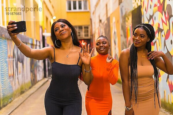 San Sebastián  Gipuzkoa Spanien  Februar 2021: Drei Mädchen machen ein Selfie. Modischer urbaner Stil mit drei schwarzafrikanischen Mädchen auf einer Stadtstraße  enge Kleider