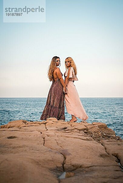 Ein paar kaukasische Mädchen mit schönen Kleidern  zeigen Zuneigung am Meer im Sommer