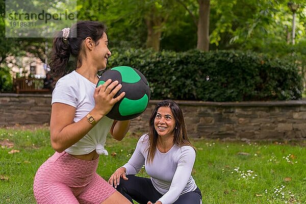 Lateinisches Mädchen beim Sport in einem grünen Park  Lebensstil ein gesundes Leben  aufmerksamer Lehrer mit den Schülern bei der Übung von Kniebeugen mit dem Gewichtsball