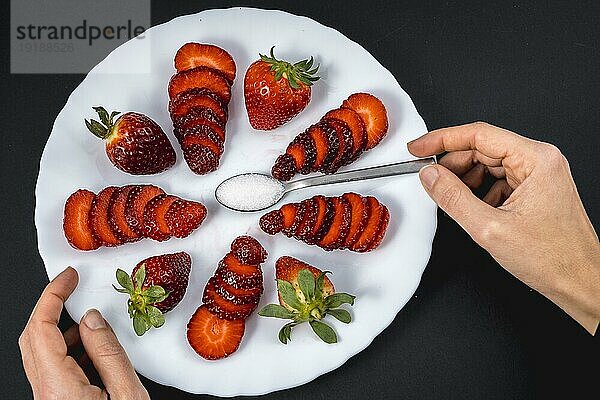 Die Hand einer Frau in einer Draufsicht auf natürliche Erdbeeren auf einem weißen Teller