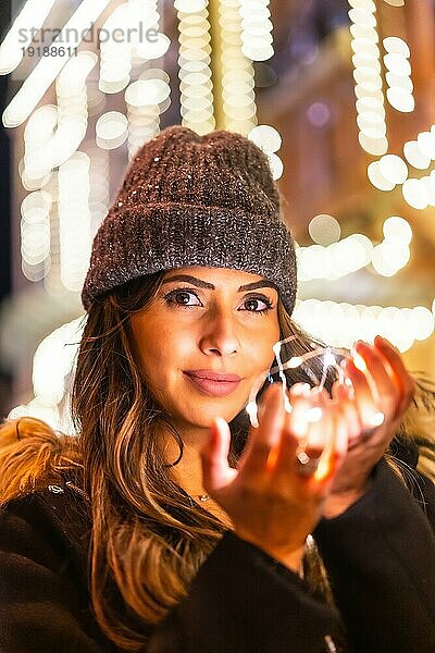 Christmas Shooting mit Weihnachtsbeleuchtung  Kaukasier in der Stadt bei Nacht mit einigen schönen Lichtern in der Hand. Mit einer Wintermütze mit Blick auf die Lichter