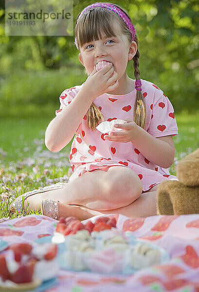 Junges Mädchen sitzt lächelnd in einem Garten und isst einen Cupcake