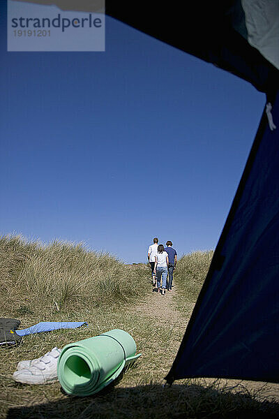 Rücken von drei gehenden Personen mit geöffnetem Zelt