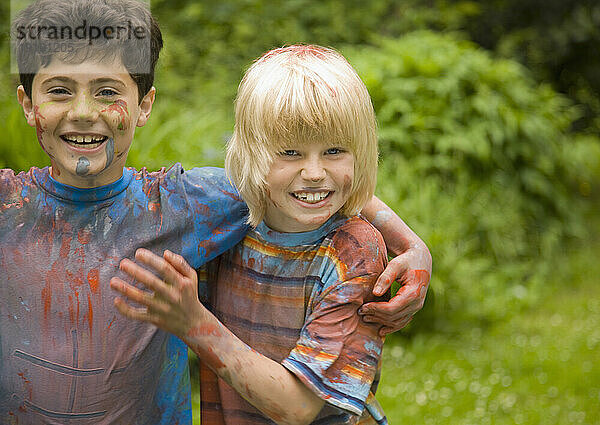 Zwei mit Aquarellfarbe bedeckte kleine Jungen lachen in einem Garten