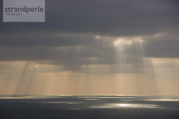 Grauer Himmel mit Sonnenstrahlen  die auf das Meer scheinen