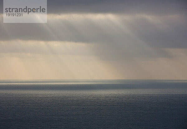 Grauer Himmel mit Regen und Sonnenstrahlen  die auf das Meer scheinen