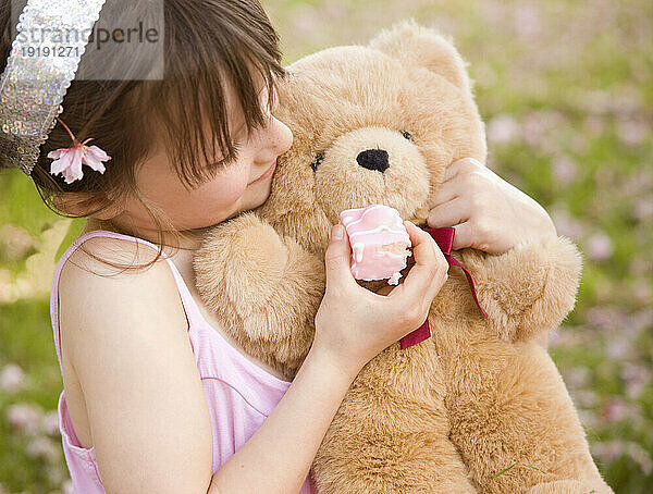 Junges Mädchen hält und füttert einen Teddybären mit Kuchen