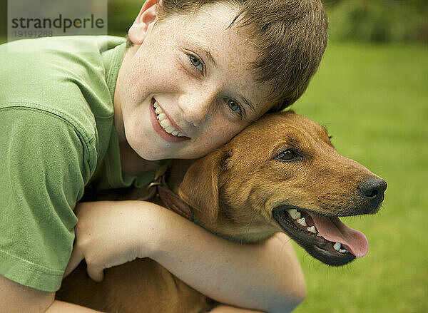 Junger lächelnder Junge umarmt seinen Hund
