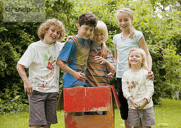Mit Aquarellfarbe bedeckte Kinder in einem Garten  zwei von ihnen stehen in einem Karton