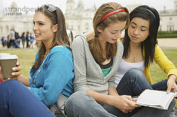 Mädchen im Teenageralter sitzen vor der London Horse Guards Parade  trinken Kaffee und lesen ein Buch