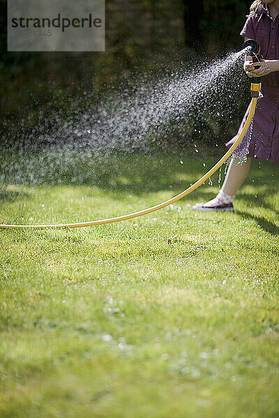 Kopfloses junges Mädchen besprüht den Rasen mit einem Gartenschlauch