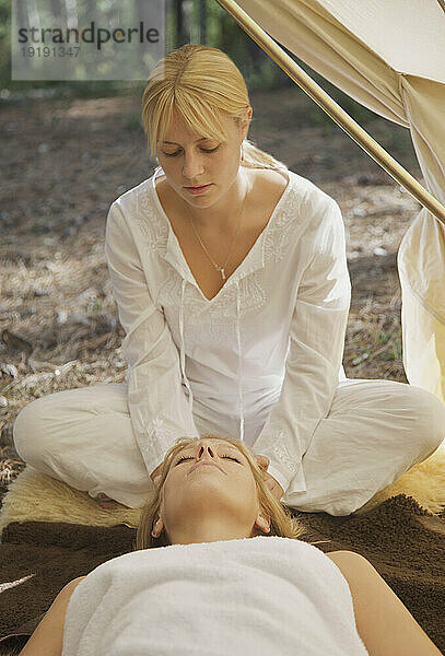 Eine Massagetherapeutin sitzt hinter einer Frau und massiert unter einem Zelt ihre Kopfhaut