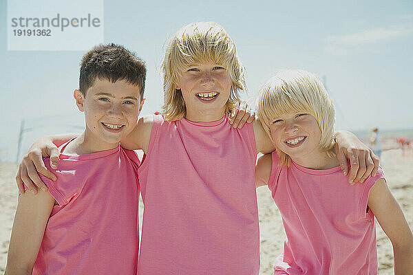 Drei lächelnde Jungen am Strand  die identische rosa T-Shirts tragen