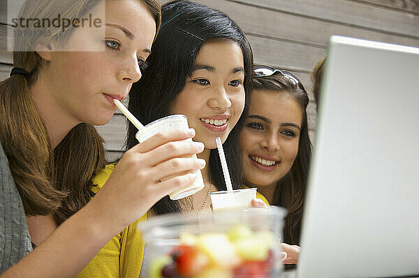 Mädchen im Teenageralter benutzen Laptop und trinken Milchshake