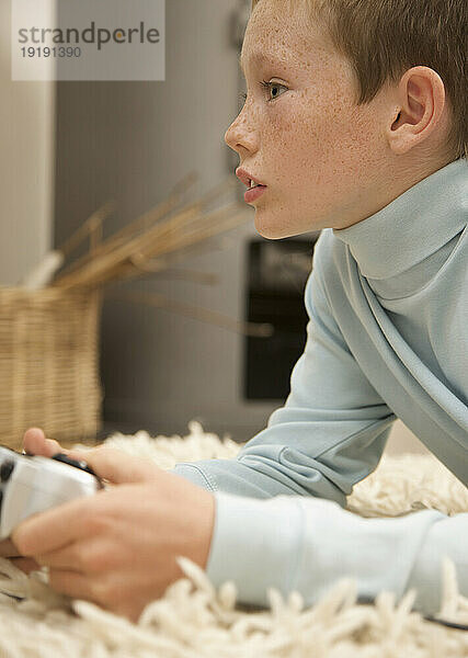 Profil eines kleinen Jungen  der auf einem Teppich liegt und eine Videospielsteuerung in der Hand hält