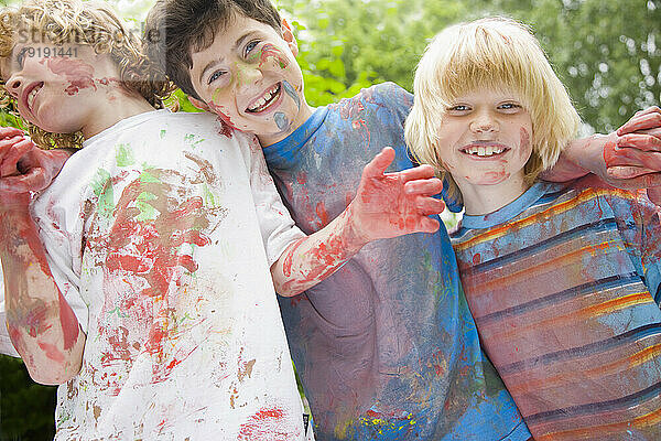 Mit Aquarellfarbe bedeckte kleine Jungen lachen in einem Garten