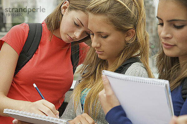 Drei Mädchen im Teenageralter lesen  schreiben und halten Notizblöcke