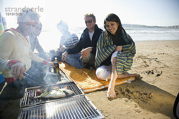 Freunde sitzen beim Grillen am Strand