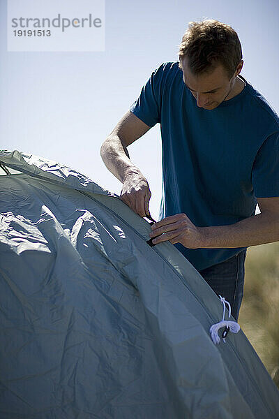 Porträt eines jungen Mannes  der steht und ein Zelt aufbaut
