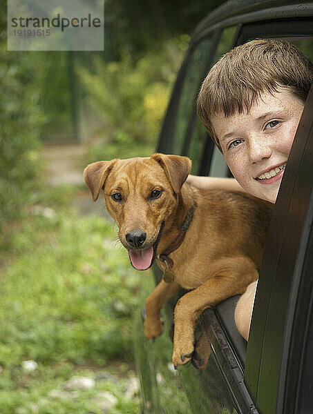 Kleiner Junge und sein Hund lehnen sich aus dem Autofenster