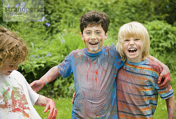 Mit Aquarellfarbe bedeckte kleine Jungen lachen in einem Garten