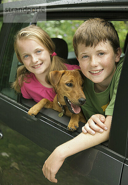 Junge und Mädchen mit Hund lehnen sich aus dem Autofenster