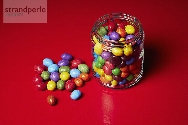Stillleben mit bunten Süßigkeiten im Glas auf rotem Hintergrund
