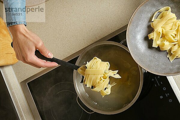 Draufsicht auf eine weibliche Hand  die gekochte Fettuccine Nudeln aus dem Kochtopf nimmt
