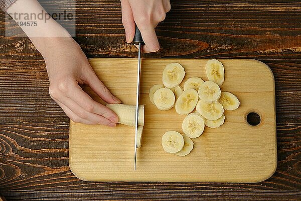 Draufsicht auf weibliche Hände  die eine frische Banane mit einem Messer schneiden