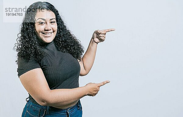 Lächelnde junge kaukasische Frau  die auf eine Beförderung hinweist  isoliert. Fröhliches Mädchen  das auf ein Angebot zeigt  isoliert. Junges Mädchen zeigt auf ein Banner an der Seite