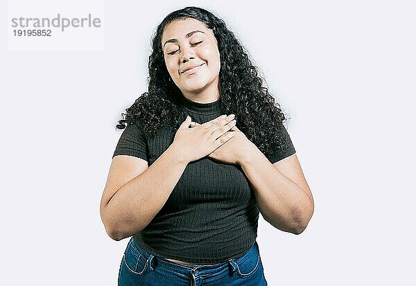 Positives lateinamerikanisches Mädchen mit Händen auf der Brust. Dankbare junge Frau mit Händen auf der Brust. Dankbares jugendliches Mädchen lächelnd mit Händen auf der Brust isoliert