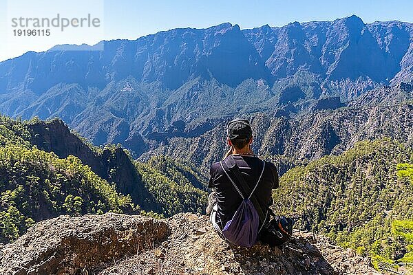 Ein junger Mann ruht sich nach einer Wanderung auf dem Gipfel des La Cumbrecita aus  sitzt auf dem natürlichen Aussichtspunkt und macht ein Foto mit dem Handy  Insel La Palma  Kanarische Inseln  Spanien  Europa