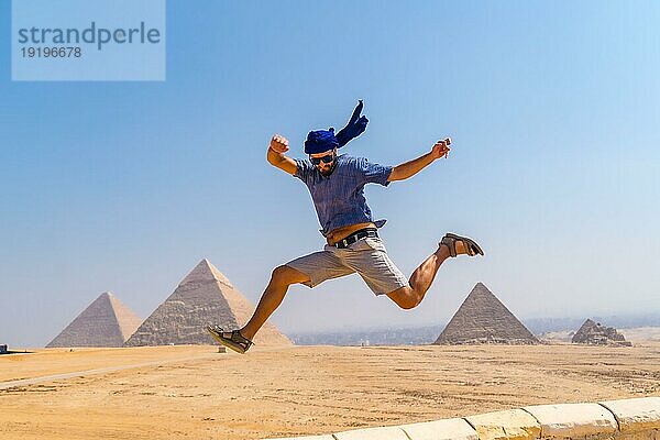 Ein junger Tourist mit blauem Turban und Sonnenbrille hüpft vor Freude bei den Pyramiden von Gizeh  dem ältesten Begräbnisdenkmal der Welt. In der Stadt Kairo  Ägypten  Afrika