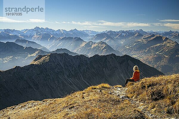 Berglandschaft  Blick vom Nebelhorn auf das Allgäu und die Alpen im Herbst. Eine Wanderin sitzt auf einem Stein neben einem Wanderweg. Gutes Wetter mit blauem Himmel  dunstig. Nebelhorn  Oberstdorf  Allgäuer Alpen  Bayern  Deutschland  Europa