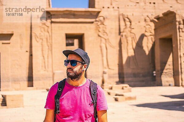 Ein junger Mann im rosa Hemd vor dem Philae Tempel  einem griechisch römischen Bauwerk  das vom Nil aus gesehen der Liebesgöttin Isis gewidmet ist. Assuan. Ägyptisch