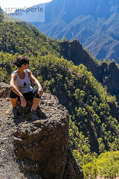 Eine junge Frau ruht sich nach einer Wanderung auf dem Gipfel des La Cumbrecita aus  während sie auf dem natürlichen Aussichtspunkt sitzt und die Berge der Caldera de Taburiente betrachtet  Insel La Palma  Kanarische Inseln  Spanien  Europa