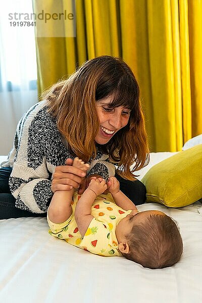 Mutter  die sich mit ihrem Baby auf dem Bett in ihrem Schlafzimmer vergnügt  junge Kaukasierin  die zum ersten Mal mit ihrem vier Monate alten Baby zusammen ist  vertikales Foto