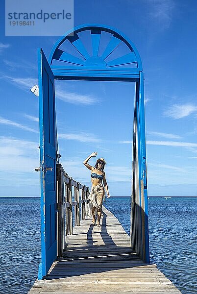 Ein fröhliches junges Mädchen vor einer blauen Tür im Karibischen Meer auf der Insel Roatan. Honduras