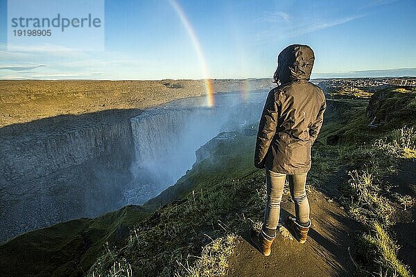 Eine junge Frau schaut sich den Dettifoss Wasserfall in Island an. Der größte Wasserfall in der europäischen Gemeinschaft
