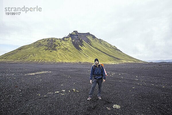 Ein junger Mann in Vulkanasche und einem grünen Berg im Hintergrund auf der 54 km langen Wanderung von Landmannalaugar  Island  Europa